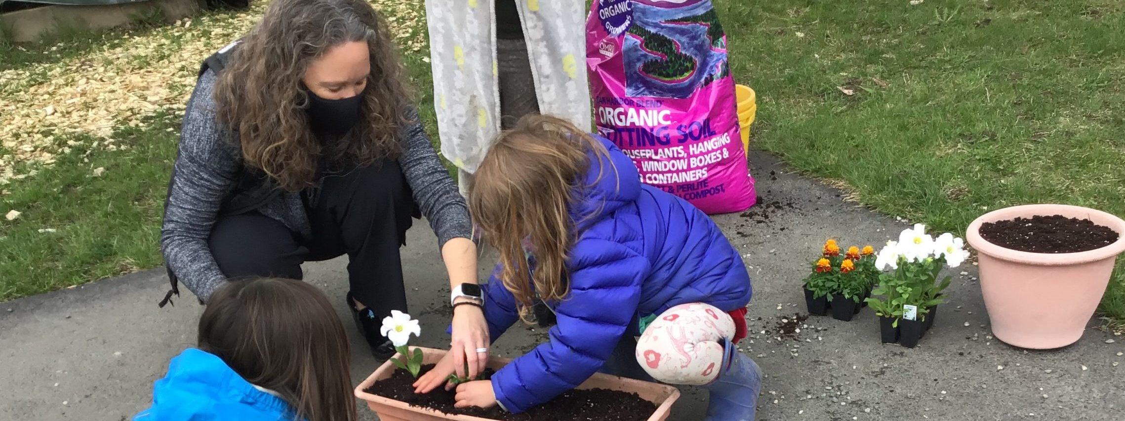 Smiling masked woman plants flowers with young children