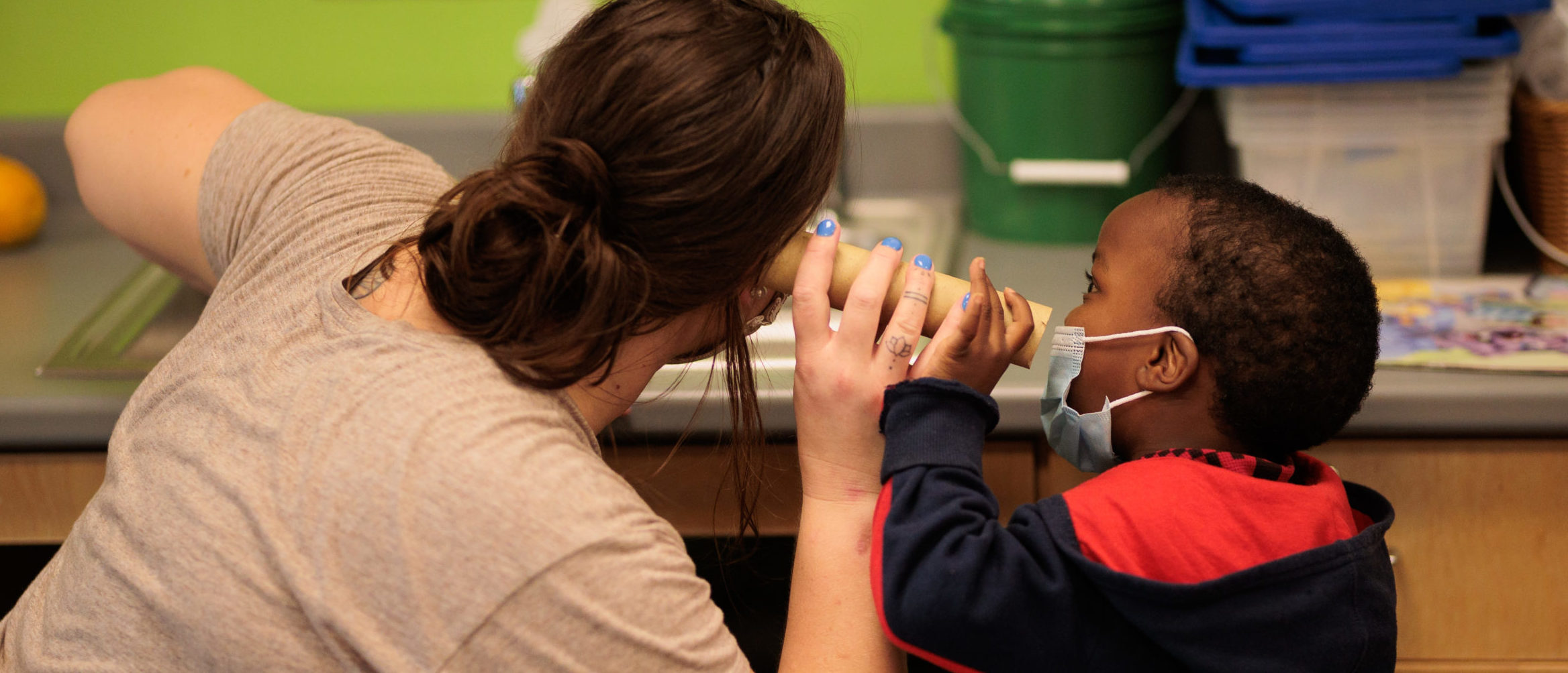 A young child pretends to talk through a block to an adult who pretends to hear through the block.