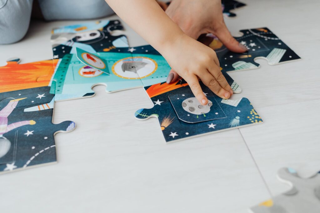 Child's hand moves a space-themed piece of a floor puzzle.