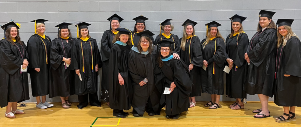 Graduates pose against a gray wall