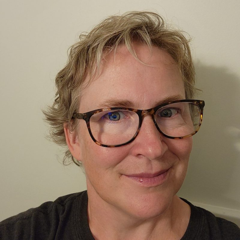BethTraverAdolphus Woman with short wavy blond hair, light skin, large glasses
