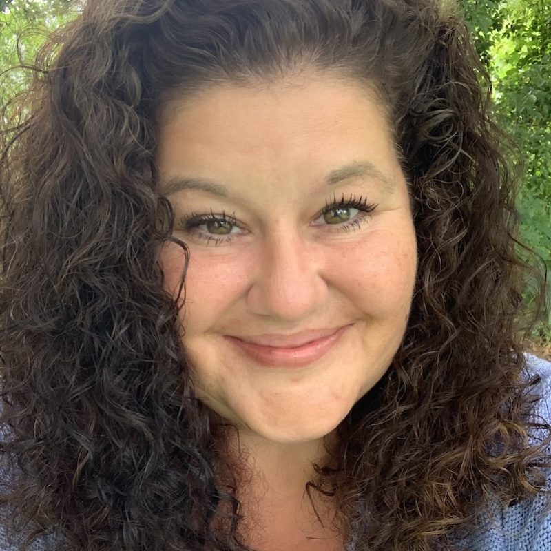 Smiling person with brown curly hair and bright blue eyes