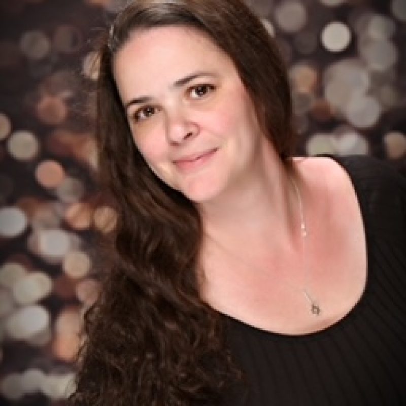 Person with long brown hair and light skin wearing a scoop neck black shirt with sparkle background
