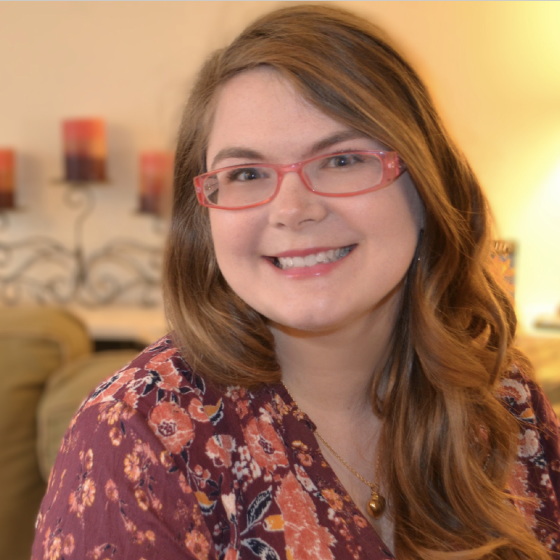CadenceDiMasi Smiling woman with long wavy brown hair, pink glasses, light skin, floral shirt, indoors